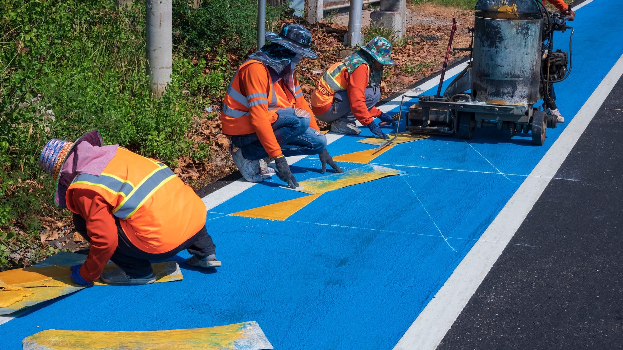 Road workers group painting traffic line and bicycle lane on asphalt road